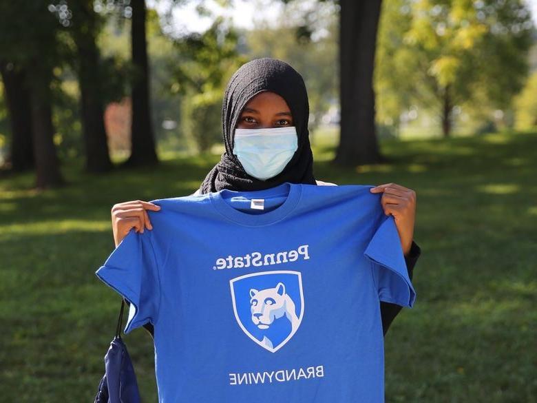 Female student wearing mask and holding up Penn State Brandywine tee shirt.