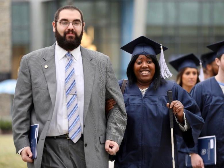 Female student walking to Commencement ceremony with male aid
